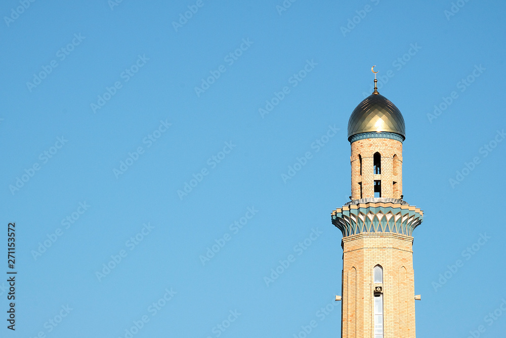 The Golden minaret of the mosque. Muslim symbol on blue sky background. Crescent. Sunset. The concept of religion.