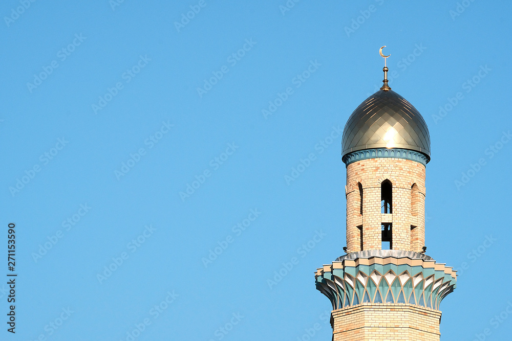 The Golden minaret of the mosque. Muslim symbol on blue sky background. Crescent. Sunset. The concept of religion.