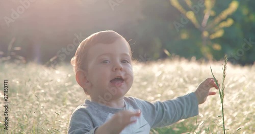 Portrait of a cute one year old boy in spring park at sunset sitting in the grass. in slow motion. Shot on Canon 1DX mark2 4K camera photo