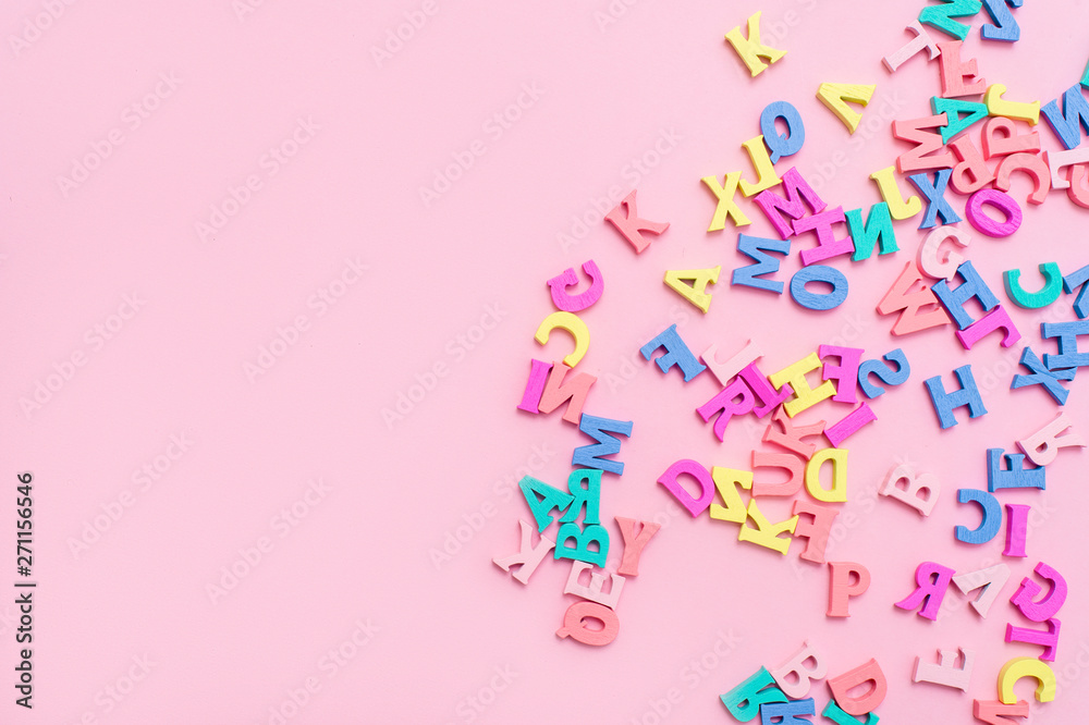 Many multicolored wooden letters on a pink background. toy letters. english alphabet. View from above. Flat lay. Copy space for text - obrazy, fototapety, plakaty 