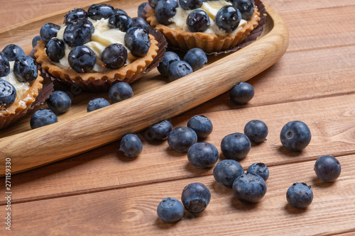 three bilberry tartlet on a wooden plate on the table, bilberry baked shells, fruit cupcake with blueberry