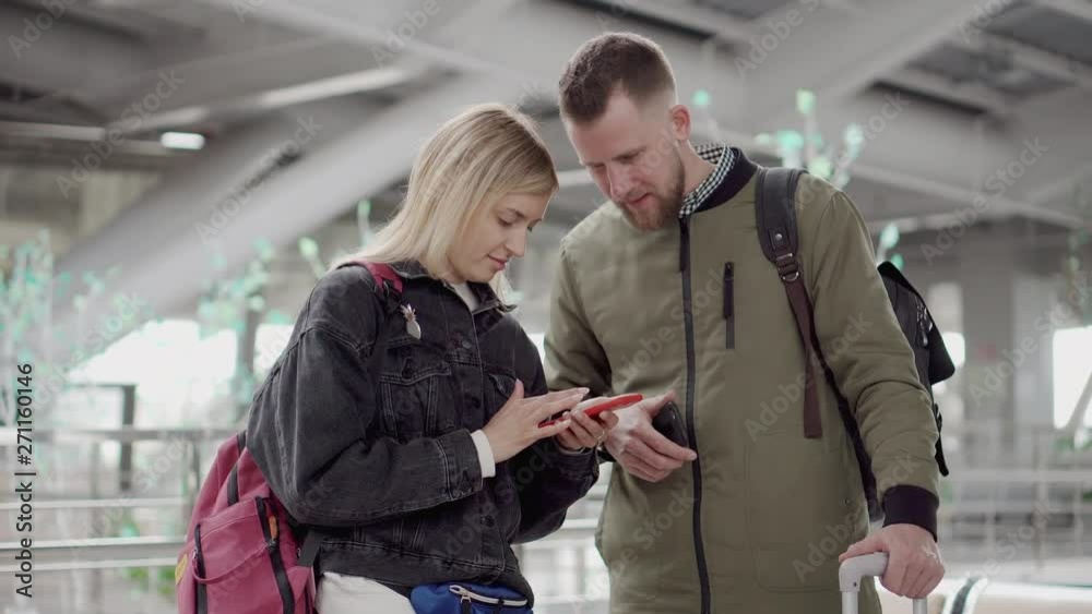 Man talking to woman while she is using smartphone in airport. Man talking to woman while she is using smartphone in airport.