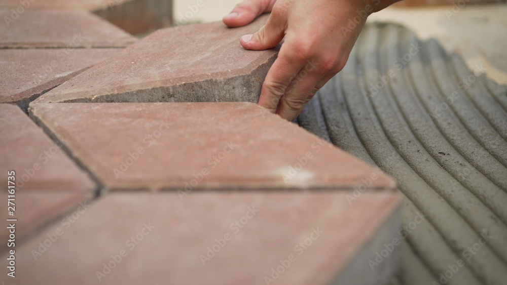 worker applies glue to tiles on pavement. worker applies glue to tiles on pavement.