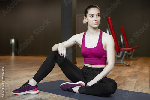 Close up portrait of young pretty european fitness woman sitting on the wooden floor at the gym. Breaking relax while exercise workout. Concept of health and sport lifestyle. Athletic Body.