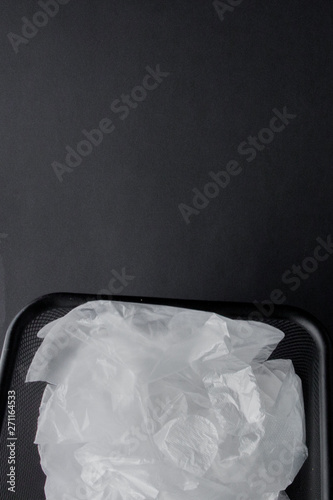 Plastic bag with handles, gloves in the bin on a black background . Used plastic bag for recycling. Concept - ecology, planet pollution with plastic cellophane polyethylene