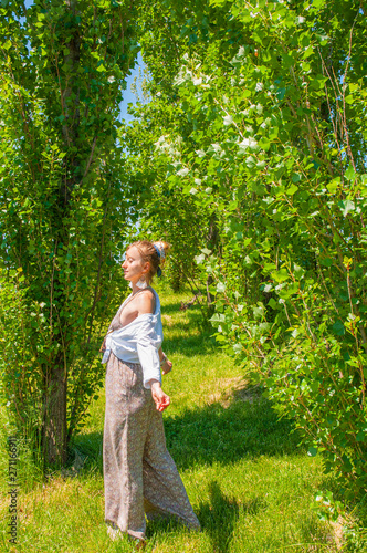 Beautiful boho style woman in fashionable jumpsuit enjoying summer time in park
