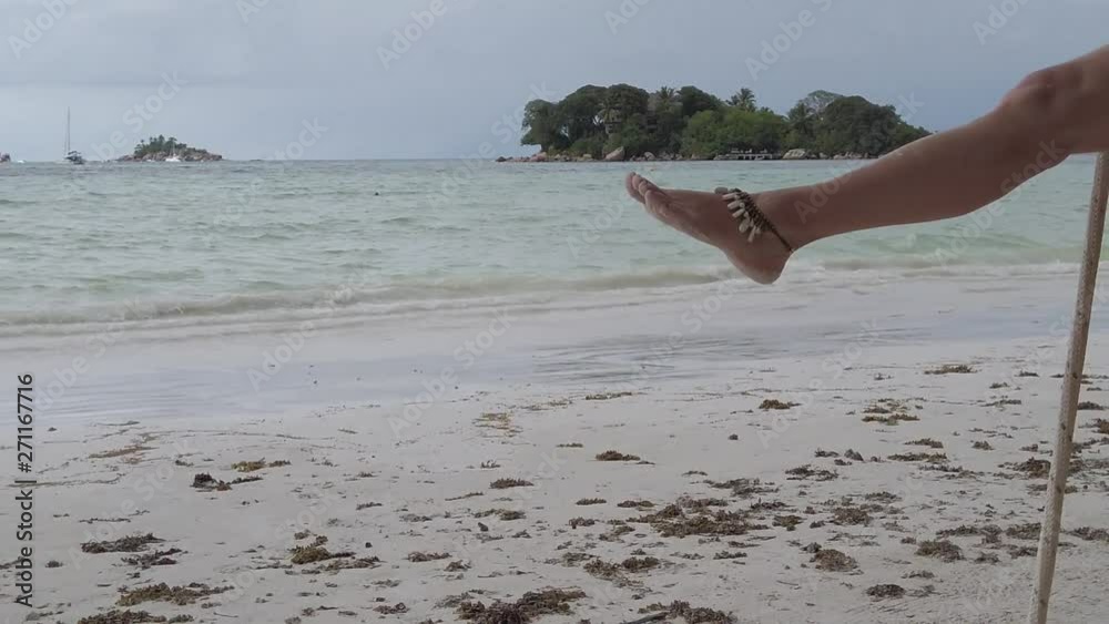 SLOW MOTION: Lifestyle tourist woman swinging on tropical beach under coconut palm trees of Anse Volbert Cote d'Or, Praslin, Seychelles, Indian Ocean. Islet of Chauve Souris on background.