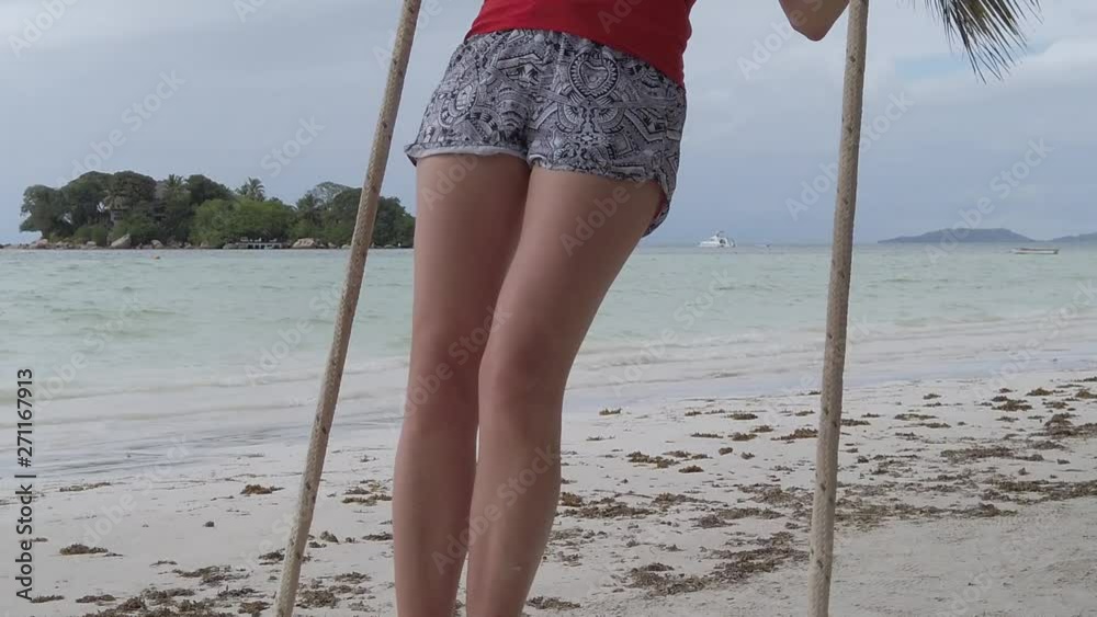 SLOW MOTION: Carefree blonde woman swinging on tropical beach Anse Volbert Cote d'Or, Praslin, Seychelles, Indian Ocean. Islet of Chauve Souris on background. Lifestyle female funny, summer vacation.