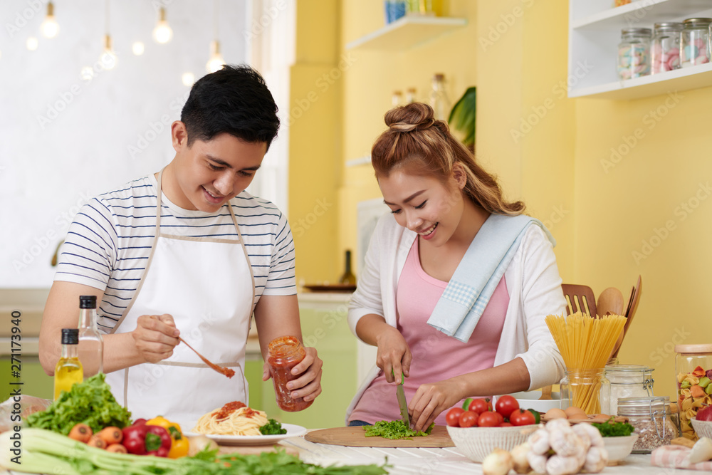 Young Vietnamese couple cooking spaghetti and salad for dinner togther