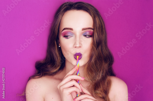 Fashion model woman creative colorful pink and blue make up. Beautiful cute girl Purple bright lips, long cerly hair. Model drinking a cocktail of paper straws. Caring for nature. Purple background.