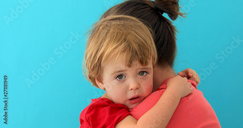 Side view of young mom cuddling sad kid looking at camera isolated on blue background