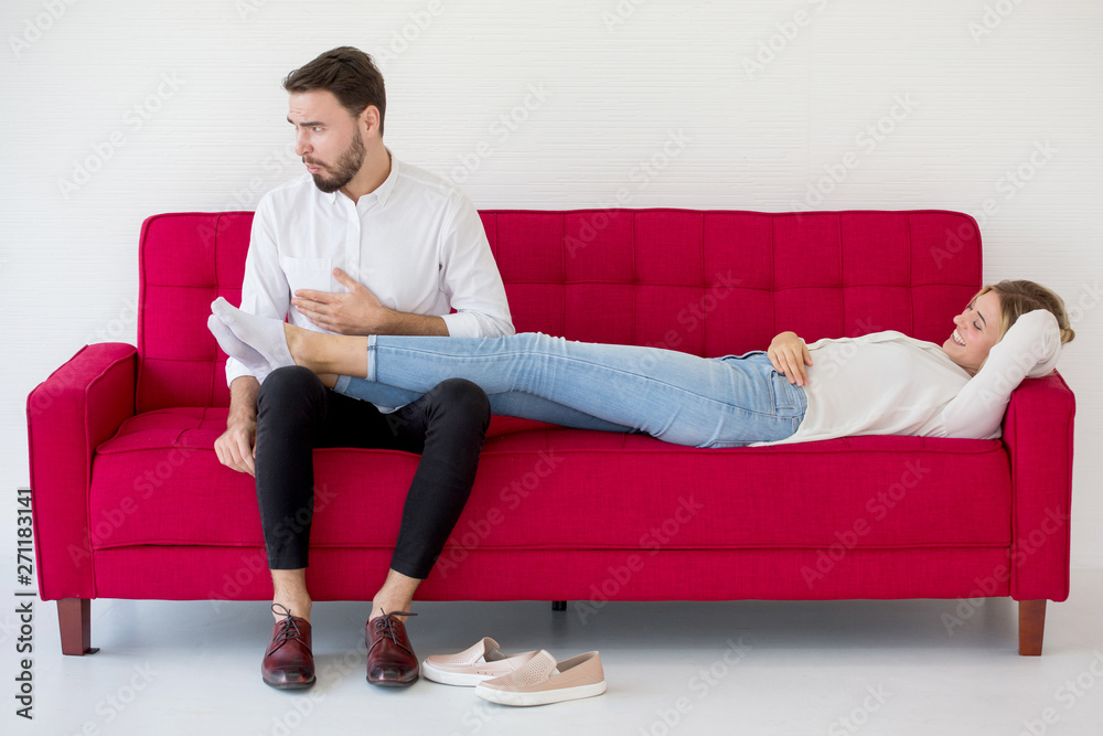 couple in love girlfriend lying down on red sofa boyfriend massage her feet with unpleasant Foot odor at home, indoors . Foul-smelling couple in love girlfriend lying down on red sofa boyfriend massage her feet with unpleasant Foot odor at home, indoors . Foul-smelling