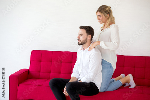 couple in love girlfriend is doing boyfriend massage shoulder on  red sofa at home, indoors