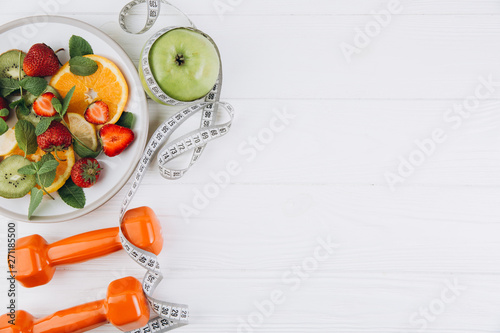 Diet plan, menu or program, tape measure, water, dumbbells and diet food of fresh fruits on white background, weight loss and detox concept, top view photo