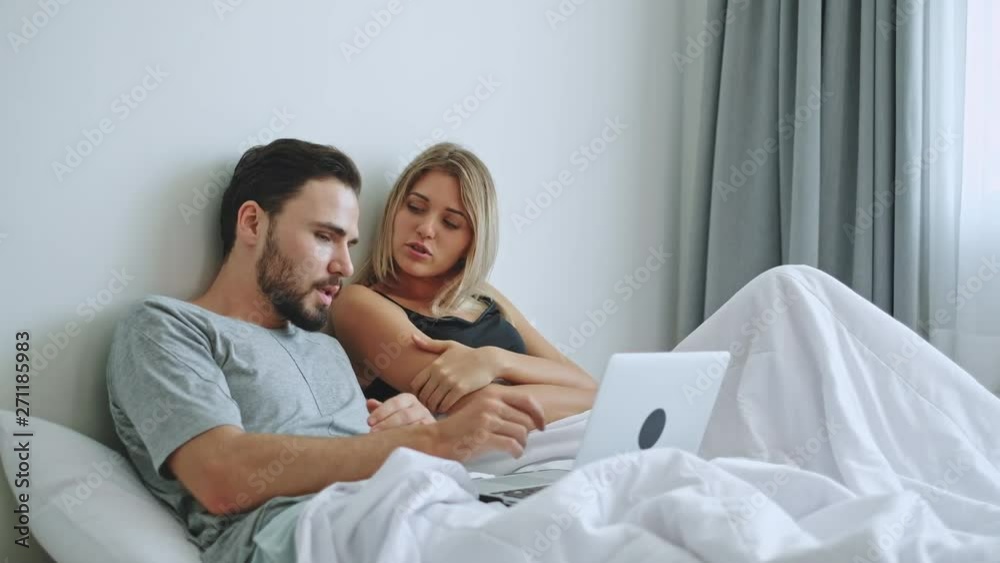 Couple lover using laptop for online shopping, internet, on white bed