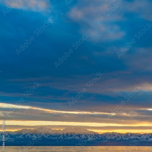 Square frame Scenic panorama of a lake and snow capped mountain under a striking cloudy sky