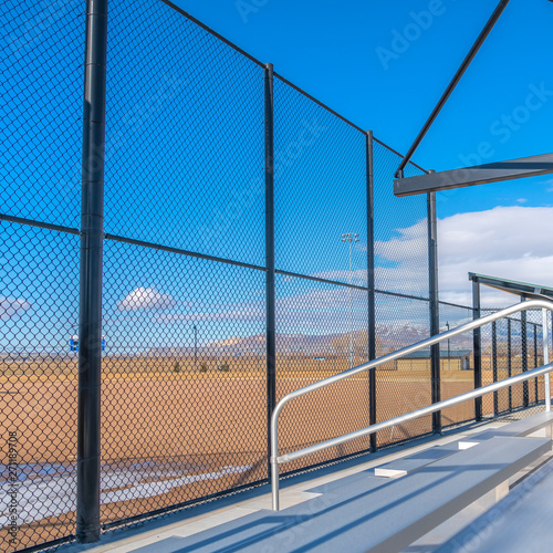 Square Sunlit bleachers overlooking a vast sports field on the other side of the fence