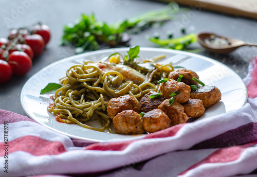 Spinach spaghetti with meatballs and egg. Green tasty pasta served with cherry tomatoes and basil