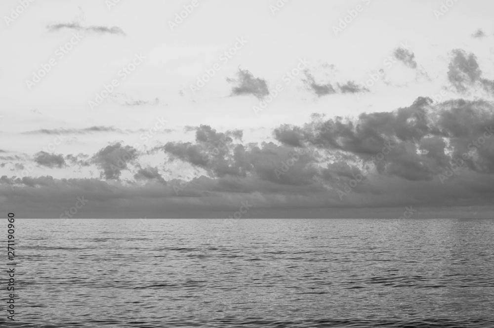 Picturesque cloudy sky seascape. High heaven with fluffy clouds. Gorgeous cloudscape above calm mirrored sea water surface. Black sea landscape in dusk. Freedom concept. Black and white photography 