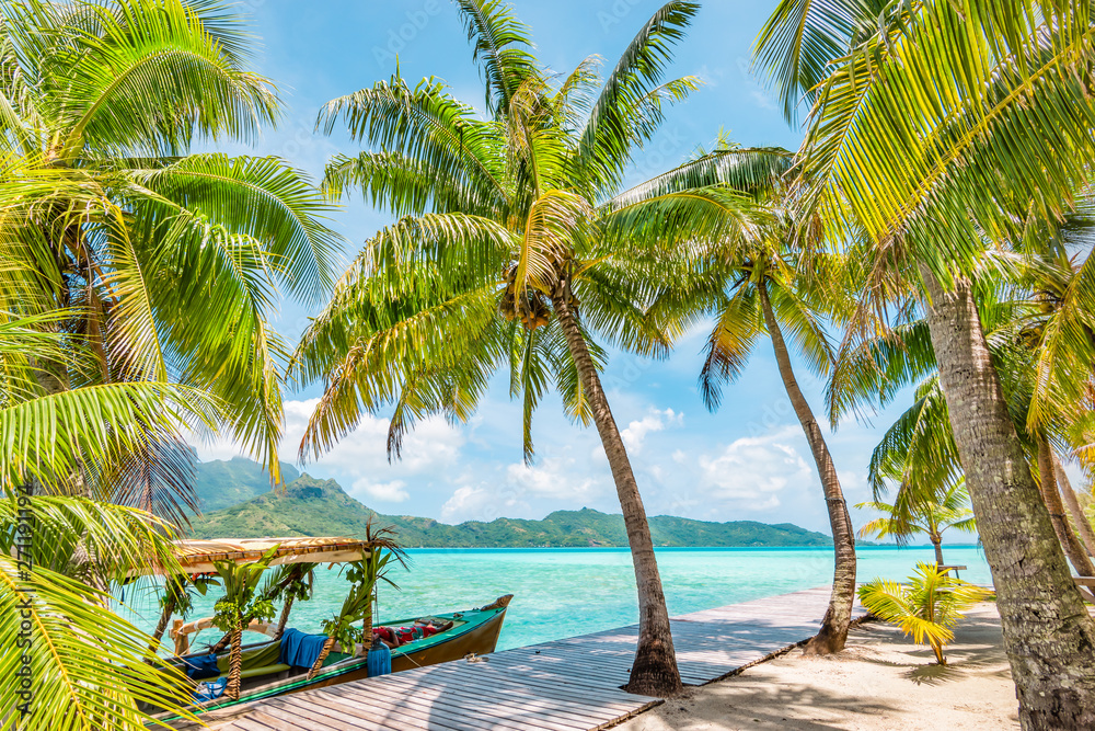 Beautiful landscape with coconut palm trees on tropical Island of Bora Bora. Decorated tourist boat moored at wooden quay.