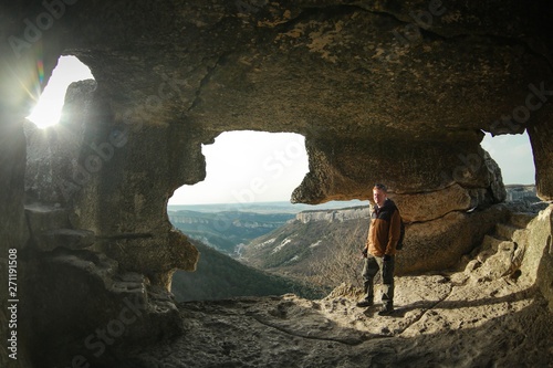 Redhead man in a brown-and-blue windbreaker stands in a cave in the cave city of Mangup-Kale in the Crimea near the city of Bakhchisaray. Travel, adventure, hiking, motivation and speleology concept.