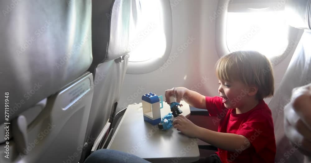 Little boy smiling and playing with toys while sitting near aircraft window during flight Little boy smiling and playing with toys while sitting near aircraft window during flight