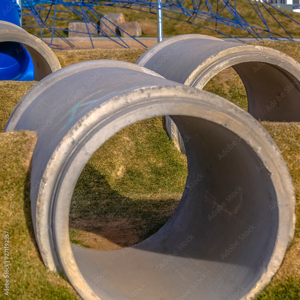Square frame Concrete tunnels between grassy mounds at a playground viewed ona sunny day Square frame Concrete tunnels between grassy mounds at a playground viewed ona sunny day