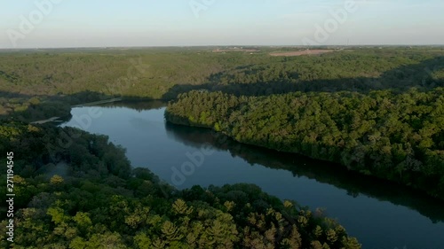 Drone shot at high altitude of a lake in the mountains surrounded by thick forest in Wisconsin, USA, during sunset. The hills cast shadows over the lake. Sky is reflecting in the water. photo