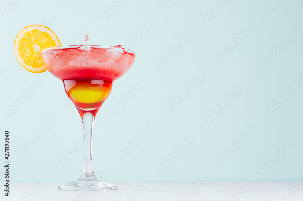 Alcohol juicy fruit red cocktail with red and yellow liquor, orange, ice cubes in wineglass in modern elegant pastel blue interior. Alcohol juicy fruit red cocktail with red and yellow liquor, orange, ice cubes in wineglass in modern elegant pastel blue interior.