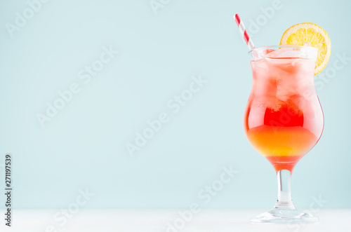 Summer cold alcohol striped cocktail with oranges juice, straw, ice cubes in luxury glass on pastel blue background, copy space.