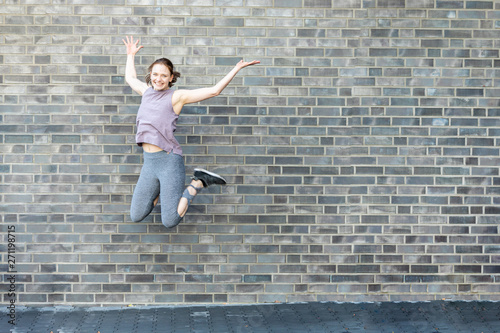 Young woman makes a jump in front of a stone wall after the workout