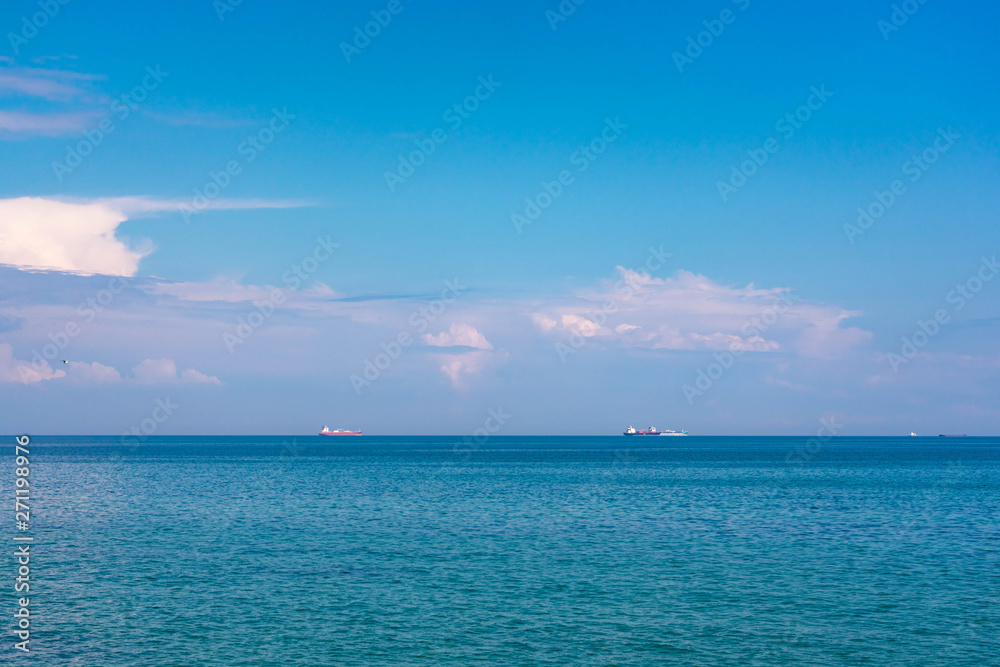 View of the Black Sea on a clear sunny day. On the shore, stones and sand, ships on the horizon. Blue sky and beautiful clouds.