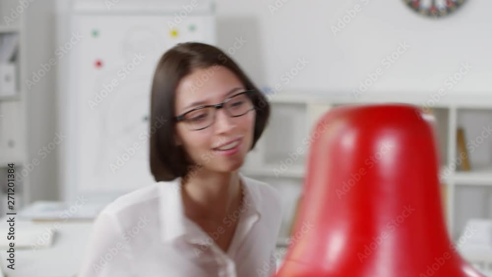 Close-up shot of 20-something vivacious female office worker, wearing white blouse and glasses, enthusiastically punching red boxing dummy on active lunch break Close-up shot of 20-something vivacious female office worker, wearing white blouse and glasses, enthusiastically punching red boxing dummy on active lunch break