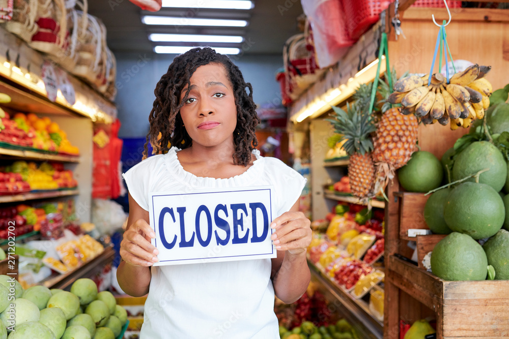 Obraz premium Sad Black young woman closing her grocery store with no customers inside