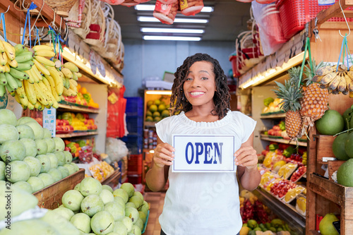 Happy excited young Black woman with signboard opening her organic grocery store