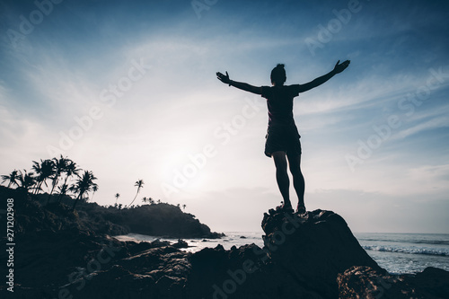 Strong woman outstretched arms on sunrise seaside rock cliff edge
