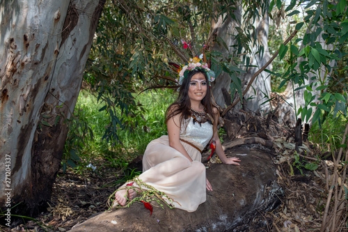 Billede på lærred Girl in the dress Pocahontas sitting on a tree trunk on the background of green