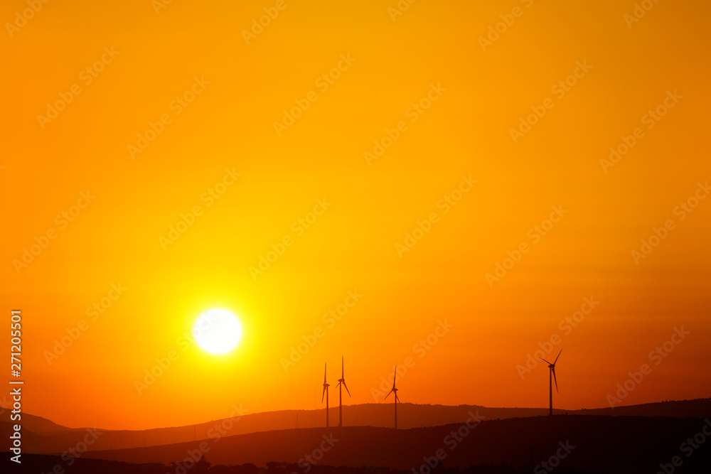 silhouetted windmills on hill over orange colored sunrise sky
