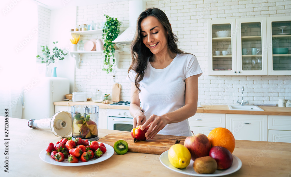 Beautiful woman making fruits smoothies with blender. Healthy eating lifestyle concept portrait of beautiful young woman preparing drink with bananas, strawberry and kiwi at home in kitchen.