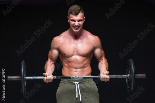 Muscular man working out in studio doing exercises with barbell at biceps, strong male naked torso abs. Isolated on black background. Copy Space. Strong tension. Sweat. Scream.