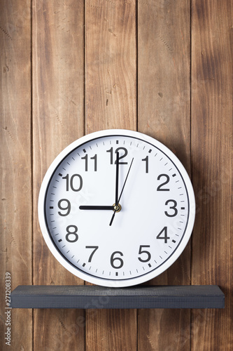 wall clock at shelf on wooden background