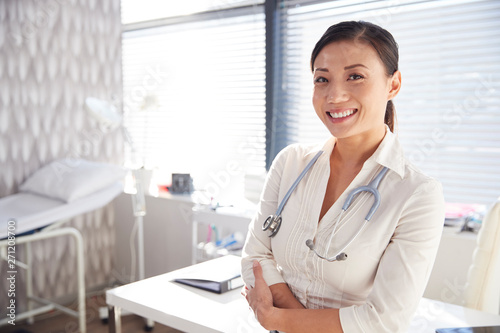 Portrait Of Smiling Female Doctor With Stethoscope Standing By Desk In Office