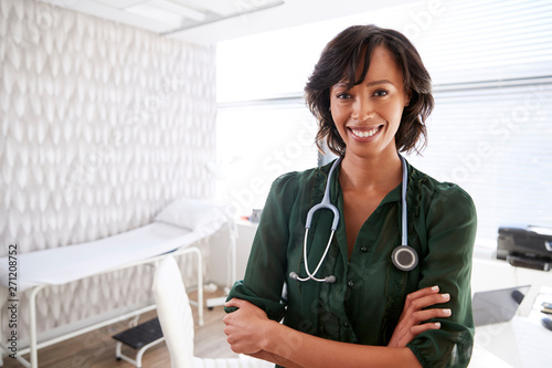 Portrait Of Smiling Female Doctor With Stethoscope Standing By Desk In Office