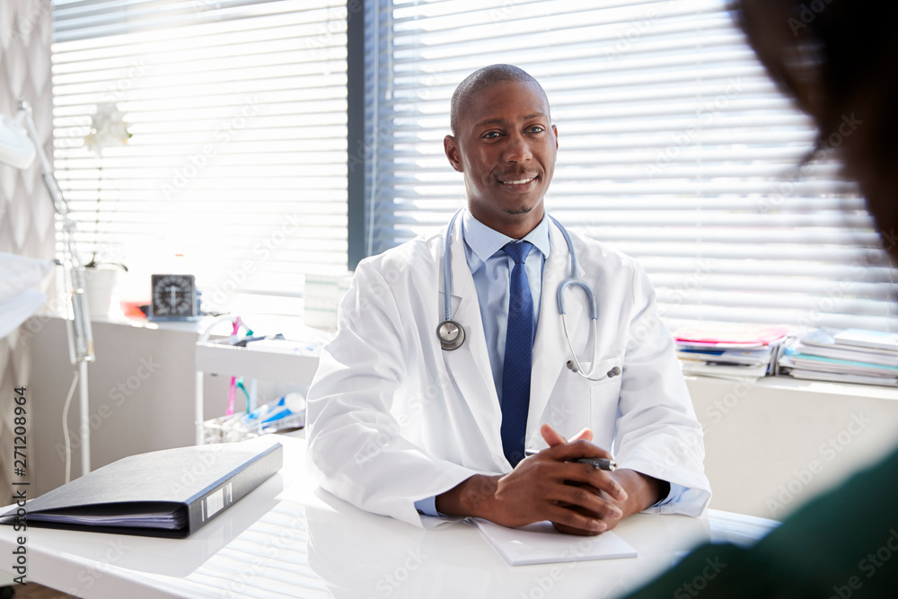 Female Patient In Consultation With Doctor Sitting At Desk In Office Female Patient In Consultation With Doctor Sitting At Desk In Office