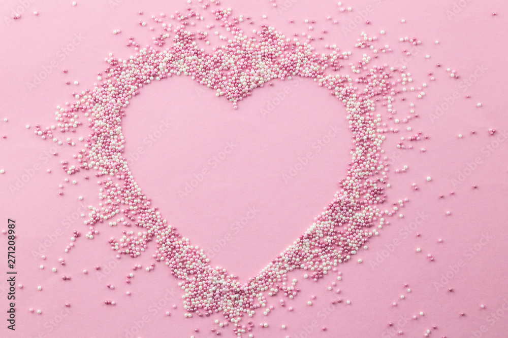 Pink and white pearly cake sprinkles shaped in a heart shape with empty space for text in the centre - Sprinkles on pink background