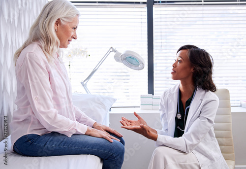 Mature Woman In Consultation With Female Doctor Sitting On Examination Couch In Office