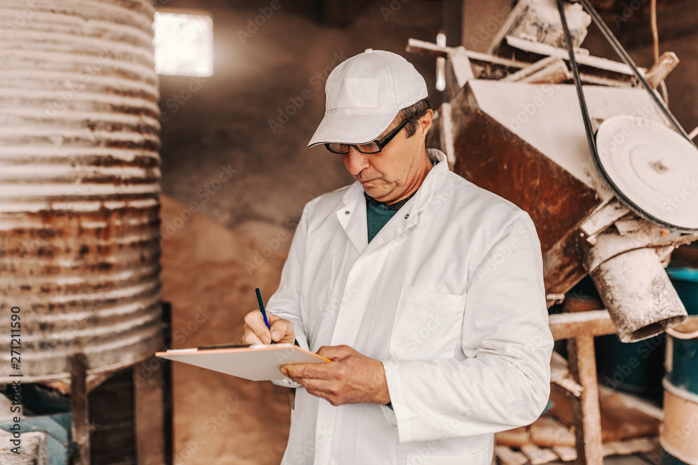 Veterinarian with cap, white uniform and eyeglasses writing results of animal examination while standing in the barn. Veterinarian with cap, white uniform and eyeglasses writing results of animal examination while standing in the barn.