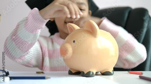 Little Asian girl putting the coin into piggy bank and smile with happiness for money saving to wealthness in the future of education concept select focus shallow depth of field photo