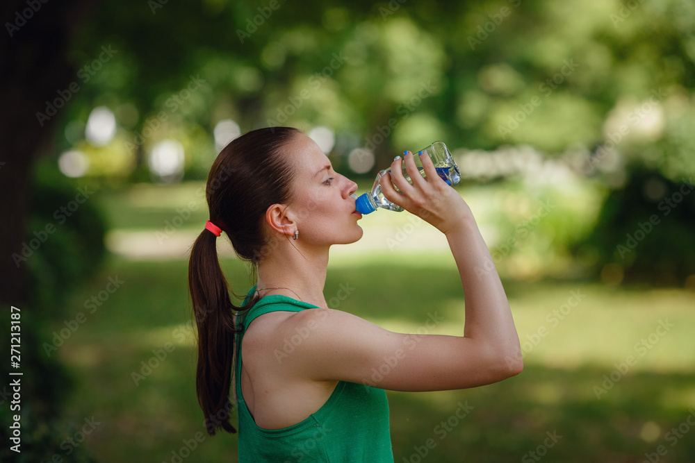 Portrait of young beautiful dark-haired woman wearing green t-shirt drinking water at summer green park. Portrait of young beautiful dark-haired woman wearing green t-shirt drinking water at summer green park.