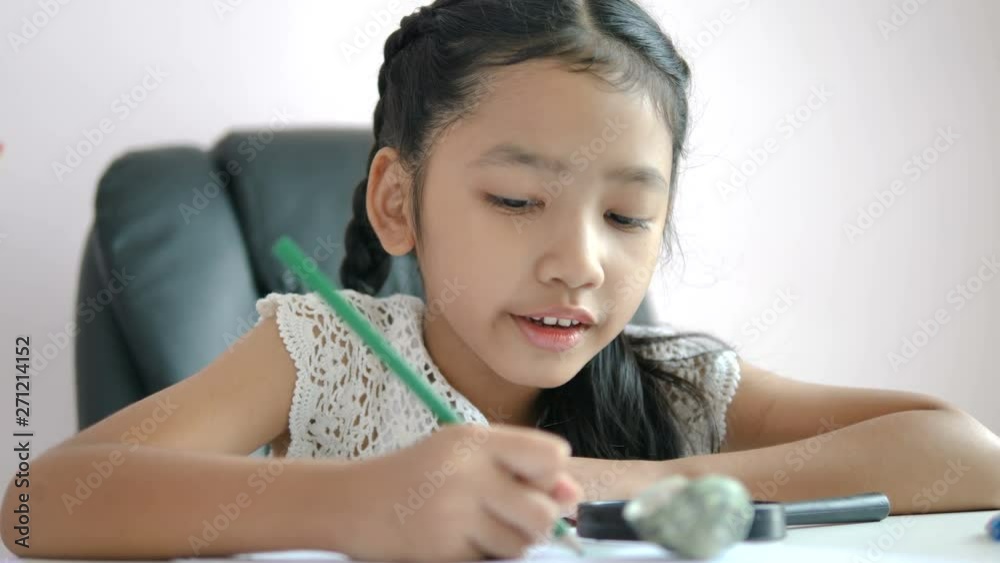 Little Asian girl using the pencil to write on the paper doing homework and smile with happiness for education concept select focus shallow depth of field Little Asian girl using the pencil to write on the paper doing homework and smile with happiness for education concept select focus shallow depth of field